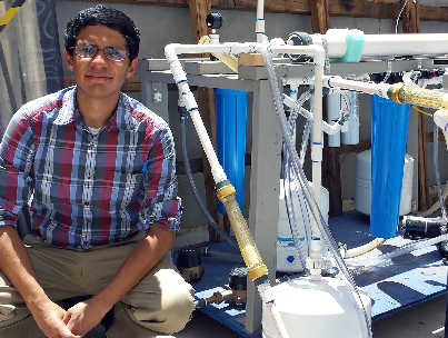 Isaac Campos, Ph.D. civil engineering student, squats among the five water filtration systems being tested as part of an interdisciplinary research effort to improve water quality in West Texas and Southern New Mexico colonias. Photo by Daniel Perez / UTEP News Service